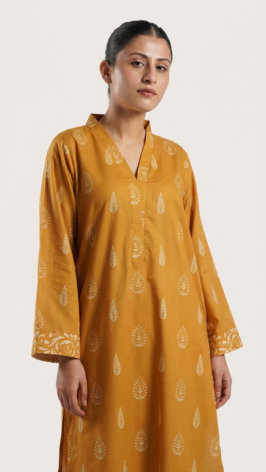 A woman wearing a mustard yellow kurta with white printed motifs and a V-neckline, photographed against a plain light background.